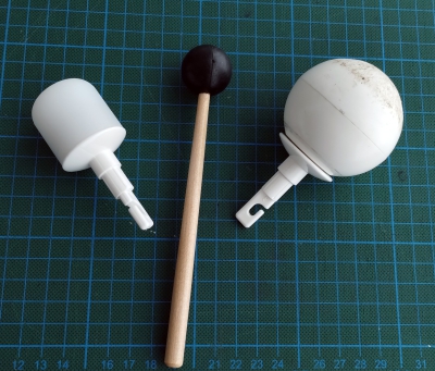 Zwei Spitzen eines Blindenlangstocks liegen auf einer Unterlage mit Gitterlinien. Dazwischen der Schlägel eines Schlagzeugs